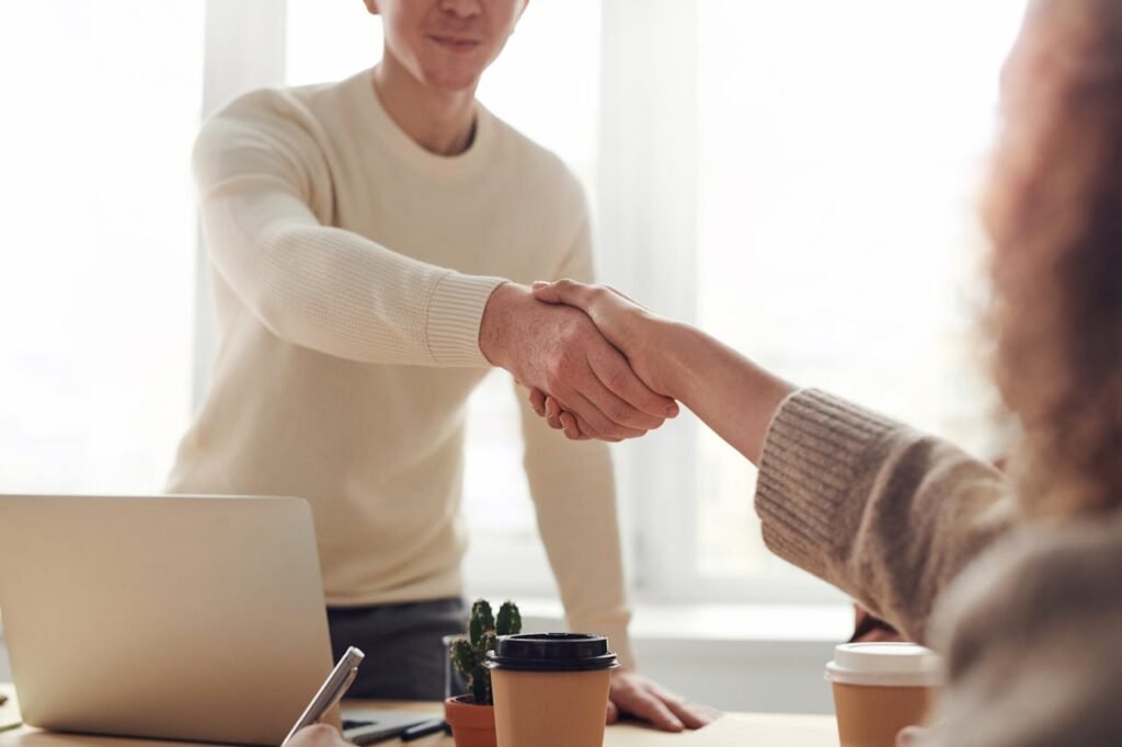 man and women shaking hands over laptop and coffee cups